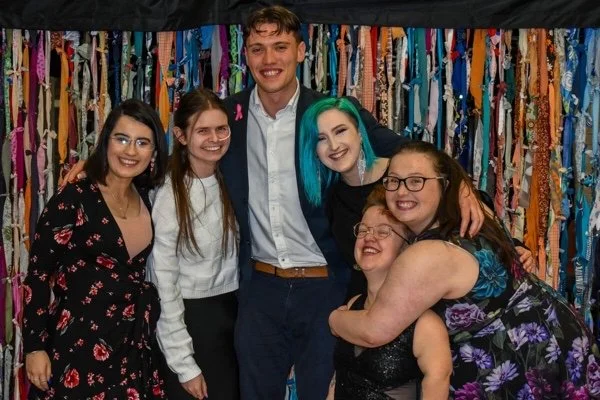 6 disabled students smiling hugging facing the camera with a multicoloured background